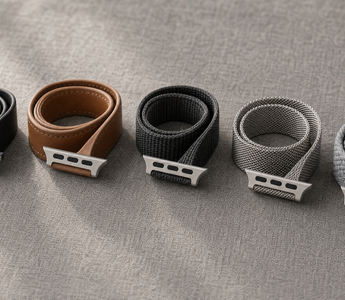Fünf aufgerollte Apple-Watch-Armbänder auf grauem Leinen: schwarzes Silikon, braunes Leder, anthrazitfarbenes Nylon, Edelstahl-Milanaise und ein graues Flechtband, jeweils mit sichtbarem Anschlussstück. Mit KI erstellte Materialdarstellung.