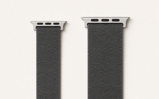 Zwei Apple-Watch-ArmbĂ€nder aus anthrazitfarbenem Nylon nebeneinander auf weiĂem Grund: links ein schmales Band der kleinen GröĂengruppe, rechts ein breiteres der groĂen Gruppe, jeweils mit dem flachen AnschlussstĂŒck. Mit KI erstellte Materialdarstellung.