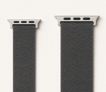 Zwei Apple-Watch-Armbänder aus anthrazitfarbenem Nylon nebeneinander auf weißem Grund: links ein schmales Band der kleinen Größengruppe, rechts ein breiteres der großen Gruppe, jeweils mit dem flachen Anschlussstück. Mit KI erstellte Materialdarstellung.