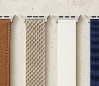 Vier Apple-Watch-Armbänder nebeneinander auf hellem Kalkstein: braunes Leder, champagnerfarbenes Milanaise-Geflecht, weißes Silikon und dunkelblaues Nylon, jedes mit dem flachen Anschlussstück. Mit KI erstellte Materialdarstellung.